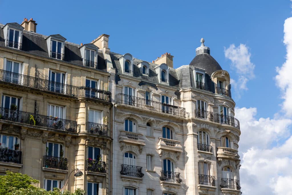 Façade haussmannienne parisienne détaillée avec balcons en fer forgé, fenêtres, toit en ardoise et dôme d'angle.